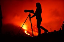 Боковой вид силуэта женщины, фотографирующей с телеобъективом и штативом лавового взрыва на Канарских островах Ла-Пальма 2021 — стоковое фото