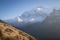 Altas laderas empinadas de montañas cubiertas de nieve ubicadas en el valle del Himalaya se extienden bajo un cielo colorido en Nepal - foto de stock
