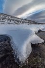 Landscape of snowy slope of hill in highland under cloudy sky in daylight and a river of ice water — Stock Photo