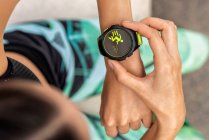 From above of crop anonymous female runner checking pulse on modern wearable fitness bracelet during workout in city — Stock Photo