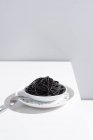 Monolocale minimalista con spaghetti neri di calamaro in ciotola di ceramica completa su tavolo bianco — Foto stock