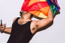 Unrecognizable homosexual male with face wrapped in rainbow flag symbol of LGBT community against white background — Stock Photo