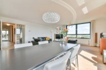Интерьер современной гостиной с цветами на столе против дивана и окна в доме в солнечный день — стоковое фото