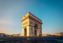 Antiguo arco de piedra con adornos y estatuas contra la plaza bajo el cielo azul al amanecer en invierno París Francia - foto de stock