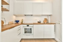 Інтер'єр кухні з білими меблями і дерев'яною стійкою і елементами в сучасній квартирі — стокове фото