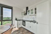 Elegante diseño interior de cocina espaciosa amueblada con armarios y electrodomésticos blancos en apartamento moderno - foto de stock