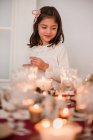 Nettes Mädchen in Kleid, das neben festlichem Tisch steht und Kerzen anzündet, um Weihnachten zu feiern — Stockfoto