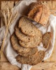 Vista superior de pedaços de pão de cereais frescos com espigões de trigo no tecido vincado na superfície de madeira — Fotografia de Stock