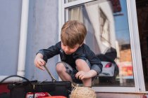 Curious kid taking wrench out of plastic container between glass door and twine ball in daytime — Stock Photo