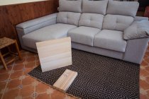 Pernas de mesa e mesa com parafusos no tapete ornamental contra sofá na sala de casa leve — Fotografia de Stock