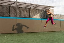 Corpo inteiro de atleta feminina duradoura em activewear pulando acima do solo durante intenso treinamento no estádio — Fotografia de Stock