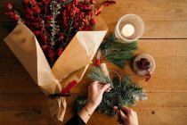 Hoher Erntewinkel unkenntlich Blumenhändlerin steht und schneidet Tannenzweige, während sie Weihnachtssträuße auf Holztisch arrangiert — Stockfoto