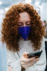 Aufmerksame Frau mit lockigem Haar und Stoffgesichtsmaske surft während der Zugfahrt mit dem Handy im Internet — Stockfoto