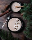 From above of black bowls with cream soup of chestnuts placed on wooden table with green branches of fir with cones — Stock Photo