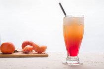 Verre de cocktail Sunrise rafraîchissant avec glaçons et paille servi sur table avec des oranges fraîches — Photo de stock