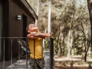 Bambino in piedi sulla veranda del cottage moderno situato nel bosco in estate — Foto stock