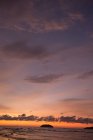 Vista panoramica del mare infinito con colline e onde che rotolano sulla riva sabbiosa sotto il cielo arancio tramonto in Malesia — Foto stock