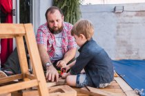 Unshaven mature dad with attentive boy measuring wooden blocks with tape while spending time on blurred background — Stock Photo