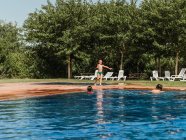 Маленький хлопчик ходить у воду з басейном, розважаючись з друзями під час літніх вихідних у сонячний день — стокове фото