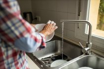 Side view of cropped unrecognizable male washing dirty plates while standing near sink in kitchen and doing housework — Stock Photo