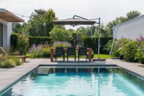 Esstisch mit Stuhl und hölzernen Liegestühlen in der Nähe des Swimmingpools im Hof einer teuren zeitgenössischen minimalistischen Villa an sonnigen Tagen — Stockfoto