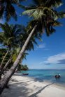 Arbres tropicaux luxuriants poussant sur la plage de sable près de transats en bois près du bateau sur l'eau azur de la mer en Malaisie — Photo de stock