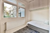 Cama confortável com cobertor em quarto de estilo minimalista com armário branco e armários em apartamento moderno com grandes janelas — Fotografia de Stock