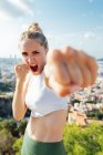 Angry female boxer shouting while showing hitting technique and looking at camera during workout in sunny city — Stock Photo