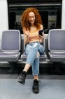 Дружелюбная женщина машет рукой во время видеочата по мобильному телефону, сидя со скрещенными ногами в поезде — стоковое фото
