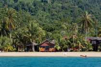 Коттеджи в окружении пышных экзотических растений на песчаном пляже, омываемом синим морем на курорте Малайзия — стоковое фото