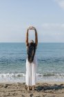 Rückansicht ethnischer Frauen, die sich im Stehen in Ashta Chandrasana zurücklehnen, während sie beim Yoga an der Sandküste gegen den Ozean posieren — Stockfoto