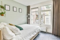 Quarto contemporâneo com almofadas em edredão entre plantas envasadas em casa com piso em azulejo — Fotografia de Stock