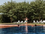 Menino caminhando na água da piscina enquanto entretendo com os amigos durante o fim de semana de verão no dia ensolarado — Fotografia de Stock
