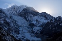 Alti ripidi pendii di montagne coperte di neve situate nella catena dell'Himalaya sotto il cielo colorato in Nepal — Foto stock