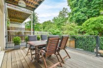Mesa de madeira e confortáveis poltronas macias colocadas na varanda de madeira da casa moderna no campo no verão — Fotografia de Stock