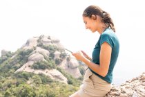 Side view of positive female tourist texting on cellphone during excursion in Montserrat mountains in Spain — Stock Photo