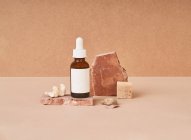 Botella pequeña de aceite de belleza y piezas de jabón natural hechas a mano con piedra pómez sobre fondo de dos colores - foto de stock