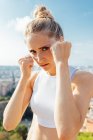 Female boxer shouting while showing hitting technique and looking at camera during workout in sunny city — Stock Photo