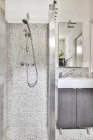 Interior do banheiro contemporâneo com cabine de chuveiro na parede de cerâmica cinza contra lavatório sob espelho em casa de luz — Fotografia de Stock