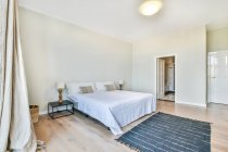 Moderno spazioso interno camera da letto en suit arredato con comodo letto con comodino vicino tappeto e bagno — Foto stock