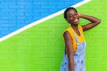 Vista lateral de la joven y feliz hembra afroamericana sonriendo mientras está de pie en la pared brillante colorido - foto de stock