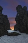 Turista con torcia su terreni sabbiosi tra montagne accidentate sotto cielo nuvoloso con stelle al tramonto — Foto stock