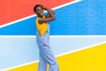 Вид на счастливую молодую афроамериканку, улыбающуюся стоя на яркой стене — стоковое фото