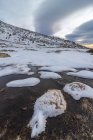 Landschaft des schneebedeckten Berghangs im Hochland unter wolkenverhangenem Himmel bei Tageslicht und einem Fluss aus Eiswasser — Stockfoto