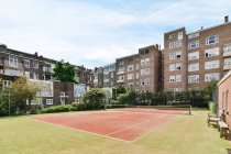 Exterior of residential buildings near empty sports court with green trees and bench under cloudy sky on sunny summer day — Stock Photo