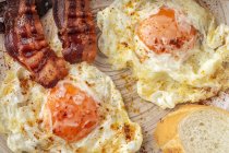 Saboroso ensolarado lado para cima ovos com tiras de bacon frito na placa — Fotografia de Stock