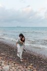 Alegre jovem fêmea dando lésbicas namorada piggyback passeio enquanto se divertindo no seixo costa contra ondulado mar no crepúsculo — Fotografia de Stock