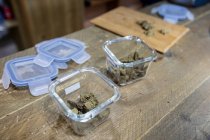 Dried hemp flower buds in transparent containers on wooden table in room on blurred background — Stock Photo