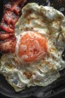Сверху на солнечной стороне яйца с жареным беконом ломтиками и приправами на темном подносе — стоковое фото
