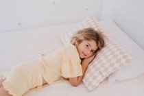 Tipo bonito criança olhando para a câmera enquanto deitado na cama em casa — Fotografia de Stock
